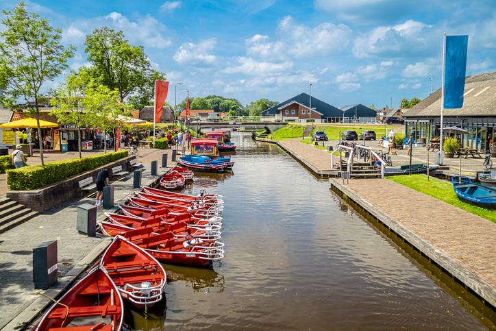 Kanal in Giethoorn mit roten Mietbooten am Ufer, Cafés, Fahnen und Gebäuden an beiden Seiten.