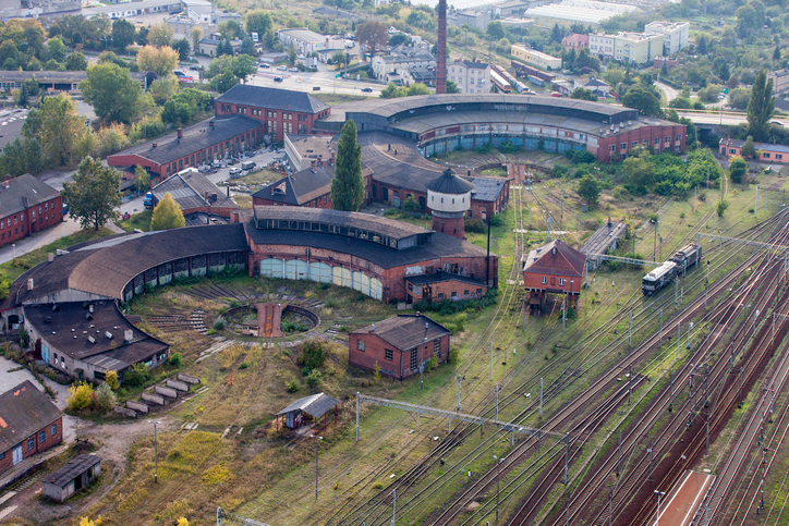 Luftaufnahme eines historischen Lokschuppens in Gniezno mit runden Backsteingebäuden, Gleisanlagen und Bahngelände.