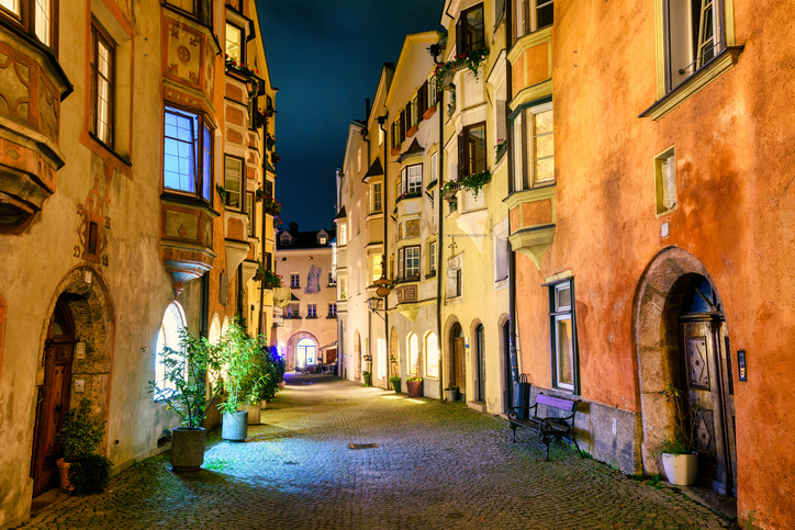 Schmale Altstadtgasse in Hall in Tirol mit warm beleuchteten Fassaden und Kopfsteinpflaster bei Nacht.
