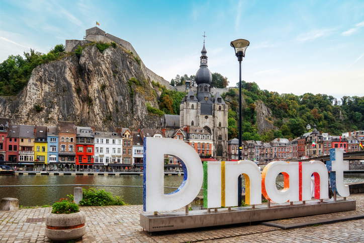 Bunter Dinant-Schriftzug an der Maas mit Blick auf die Zitadelle, die Stiftskirche und die Altstadt von Dinant.