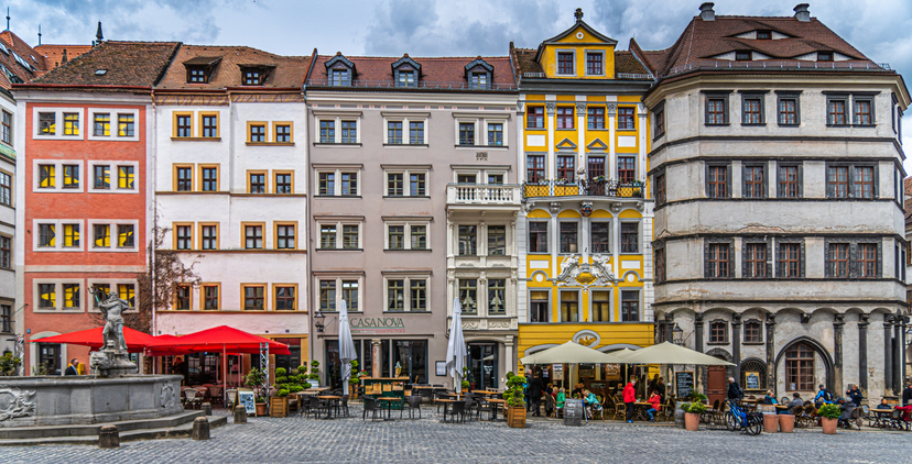 Historische Häuserfassaden am Platz in Görlitz mit Cafés, Außengastronomie, Pflastersteinen und einem Brunnen im Vordergrund.
