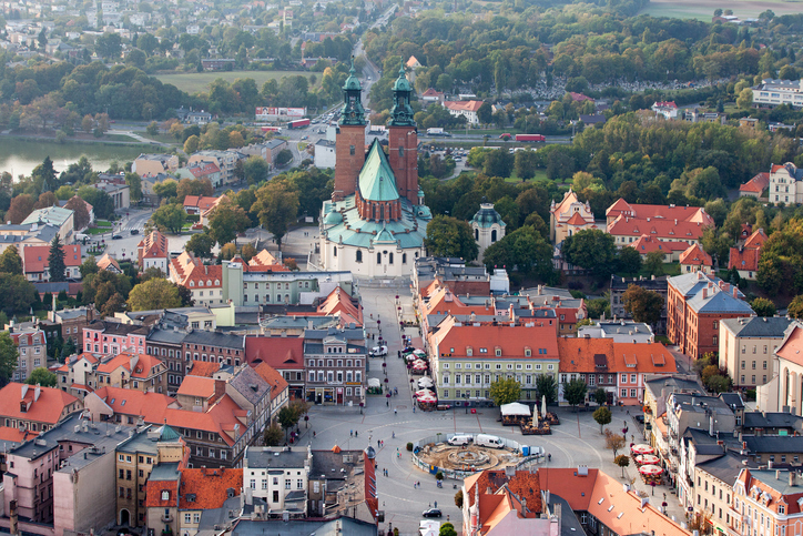 Luftaufnahme von Gniezno mit Marktplatz, Altstadthäusern und der Kathedrale von Gniezno im Hintergrund.