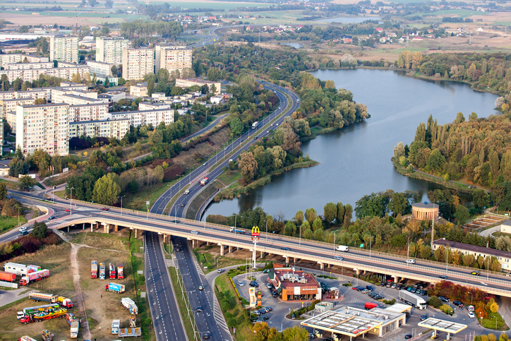 Luftaufnahme von Gniezno mit See, Straßenbrücke, mehrspuriger Straße, Wohnblocks und grünen Uferbereichen.