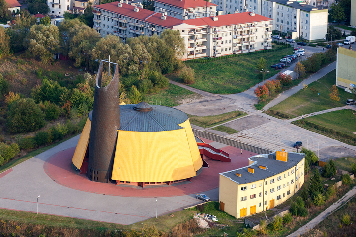 Luftaufnahme einer modernen Kirche in Gniezno mit gelbem Dach, hohem Turm und Wohnhäusern in der Umgebung.