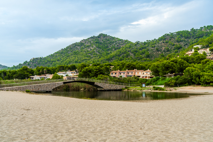 Kleine Brücke über einen Flusslauf am Strand von Canyamel mit Bergen im Hintergrund