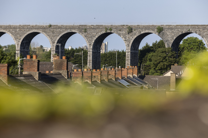 Steinernes Viadukt mit mehreren großen Bögen bei Drogheda, gesehen über Hausdächer hinweg unter klarem Himmel.