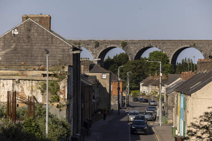 Wohnstraße in Drogheda mit geparkten Autos und einem steinernen Viadukt mit hohen Bögen im Hintergrund.