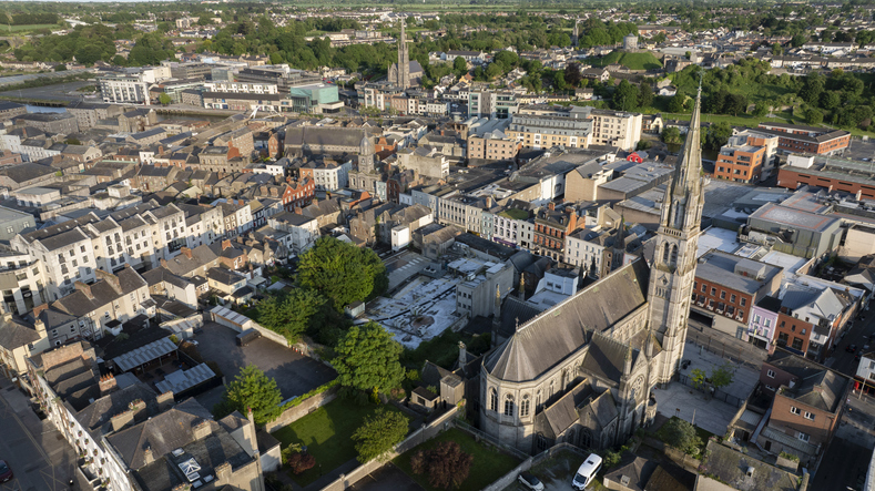 Luftaufnahme von Drogheda mit einer großen Kirche im Vordergrund, dicht bebauten Straßen und weiteren Kirchtürmen im Hintergrund.