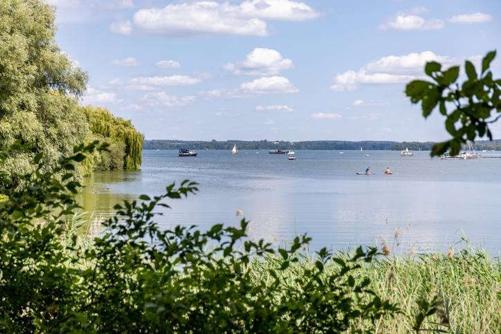 Zwischen Bäumen und Schilf öffnet sich der Blick auf einen ruhigen See mit kleinen Booten bei Schwerin.