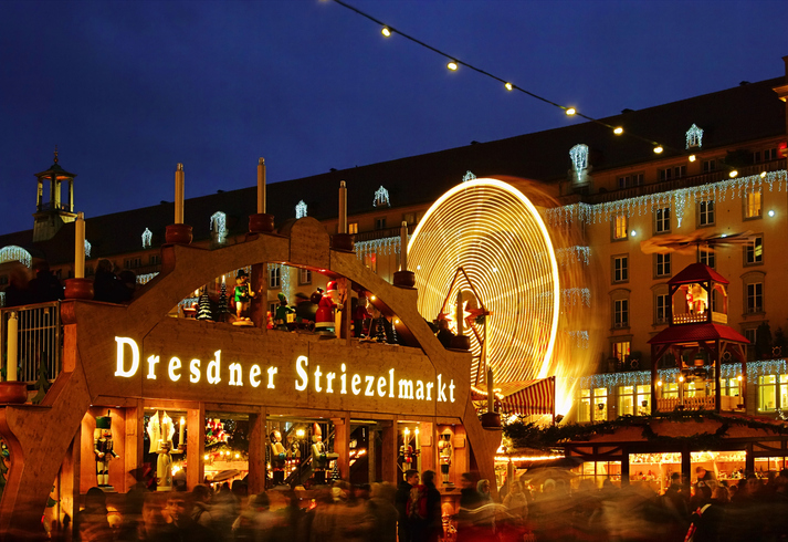 Dresdner Striezelmarkt mit beleuchteten Weihnachtsständen, großem Lichterrad, festlicher Dekoration und zahlreichen Besuchern am Abend.