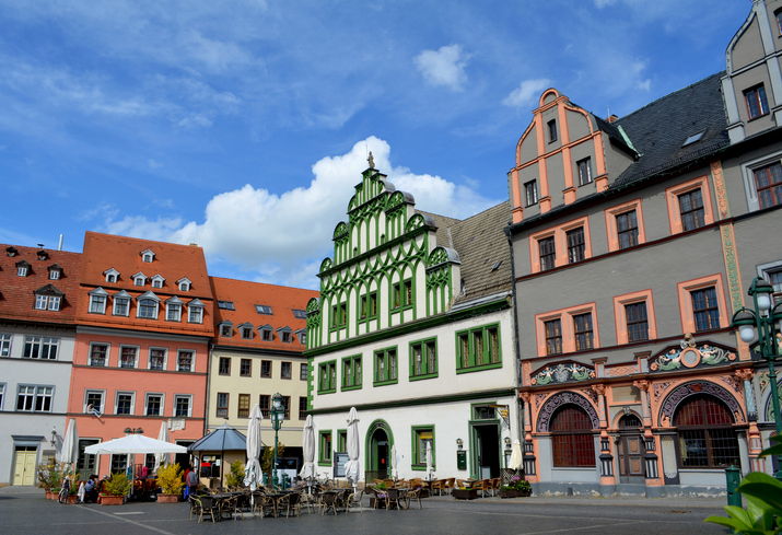 Bunte historische Bürgerhäuser mit Cafés und Außensitzplätzen stehen an einem Platz in Weimar.