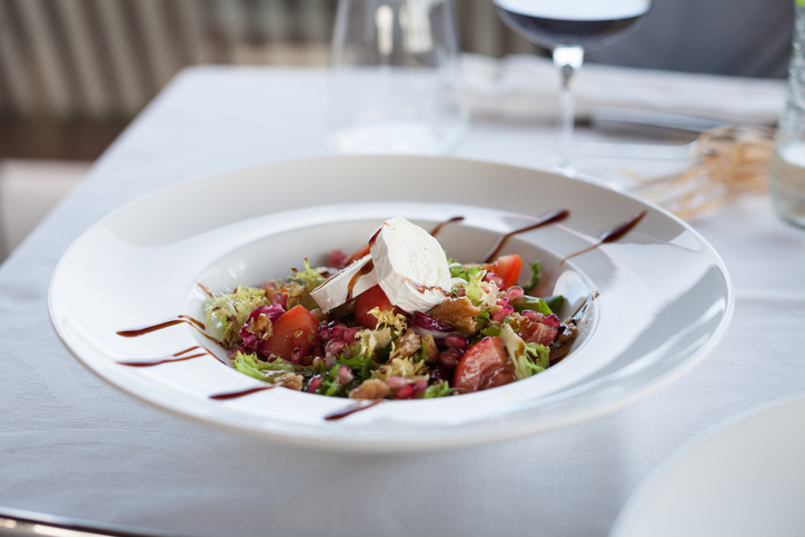 Frisch angerichteter Salat in Modena mit Blattsalat, Tomaten, Käse, Granatapfelkernen und dunklem Balsamico-Dressing auf einem weißen Teller.
