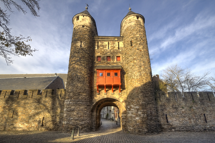 Mittelalterliches Stadttor Helpoort in Maastricht mit zwei runden Steintürmen, rotem Erker und massiver Stadtmauer.