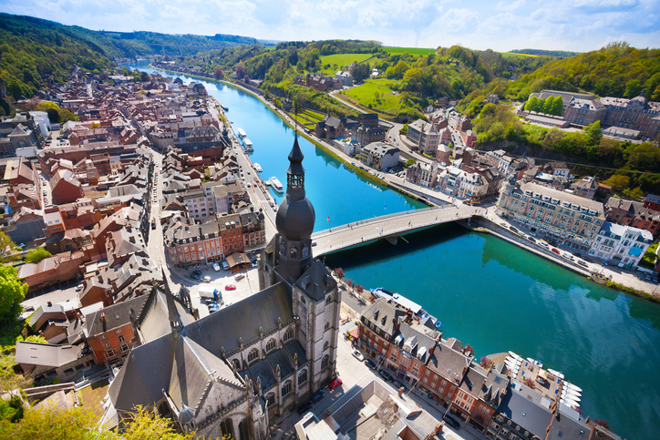 Luftaufnahme von Dinant mit Maas, Brücke, Kirchturm und dicht bebauter Altstadt.