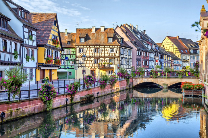 Ein geschwungener Kanal führt durch die Altstadt von Colmar, gesäumt von Fachwerkhäusern und leuchtenden Blumenkästen.