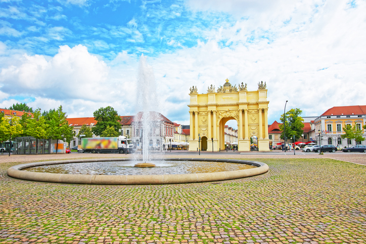 Brandenburger Tor in Potsdam am Luisenplatz mit großem Springbrunnen, gepflastertem Platz und historischen Gebäuden unter blauem Himmel.