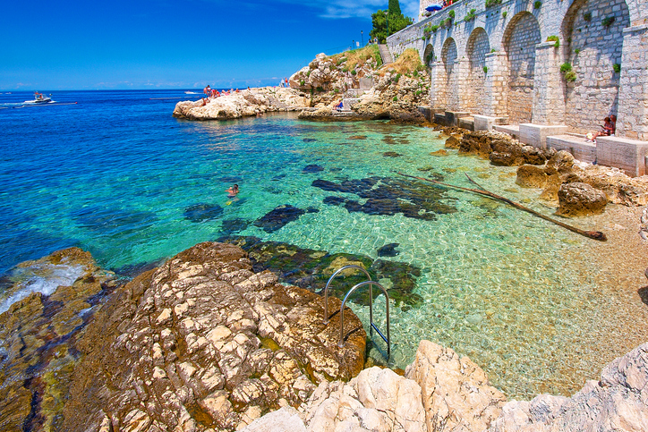 Felsige Badebucht mit klarem Wasser und steinerner Ufermauer in Rovinj