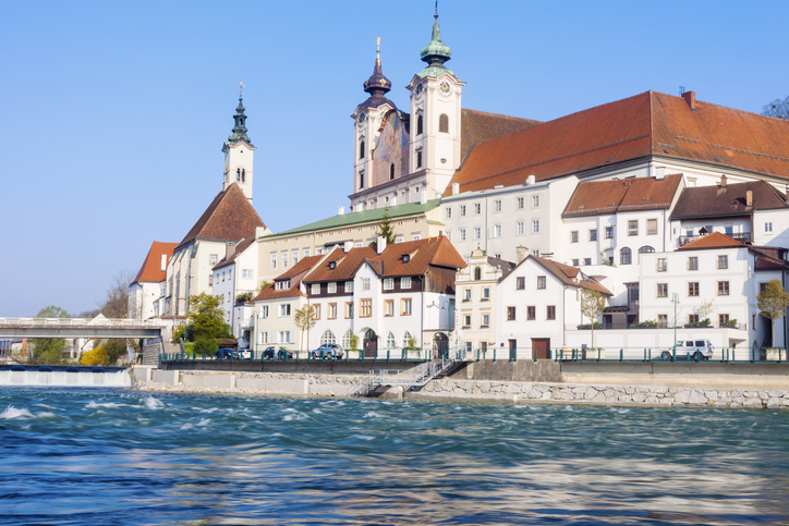 Historische Klosteranlage und Altstadthäuser am Ufer der Enns in Steyr bei sonnigem Wetter.