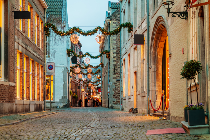 Kopfsteinpflastergasse in Maastricht mit historischen Fassaden, warm beleuchteten Schaufenstern und festlicher Dekoration über der Straße.