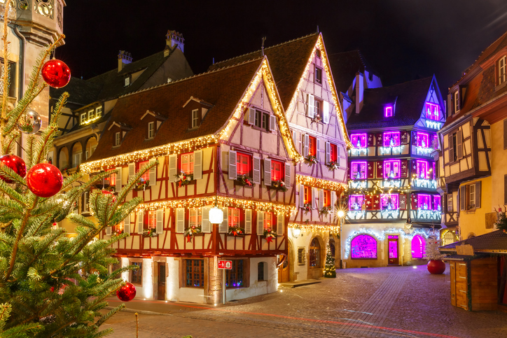 Fachwerkhäuser und bunte Blumen säumen einen Kanal in Colmar, während sich die Fassaden im Wasser spiegeln.