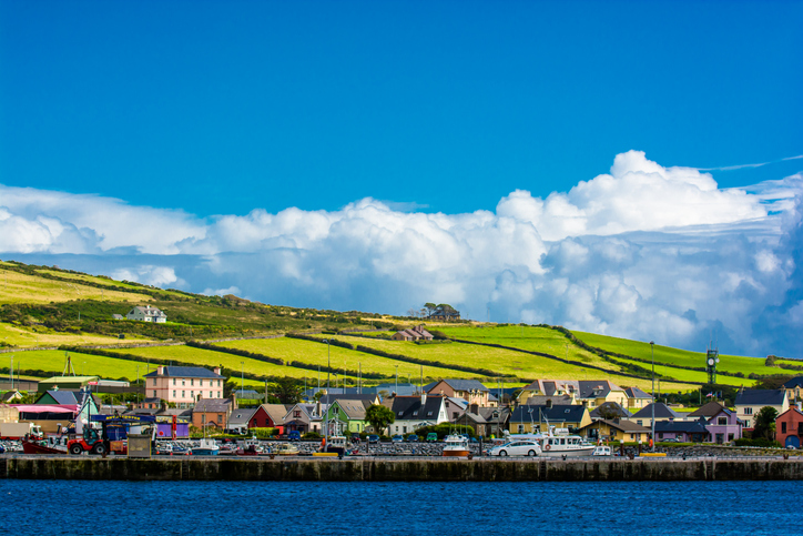 Blick über das Wasser auf Häuser und grüne Hänge am Hafen von Dingle