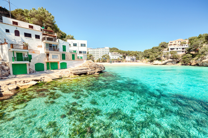 Weiße Bootshäuser mit grünen Türen am türkisfarbenen Wasser der Cala Santanyí