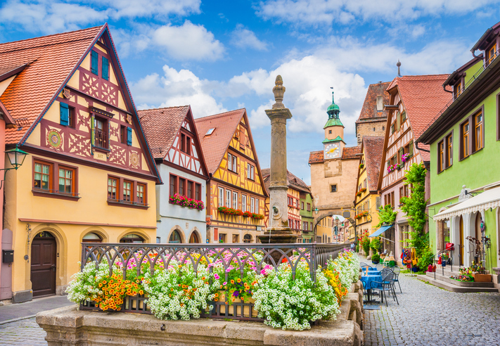 Das berühmte Plönlein in Rothenburg ob der Tauber mit Fachwerkhäusern, Brunnen, Blumen und dem Stadttor im Hintergrund.