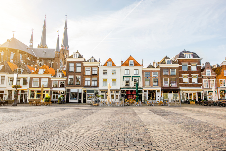 Eine Reihe historischer Giebelhäuser und Cafés säumt einen großen gepflasterten Platz in Delft.