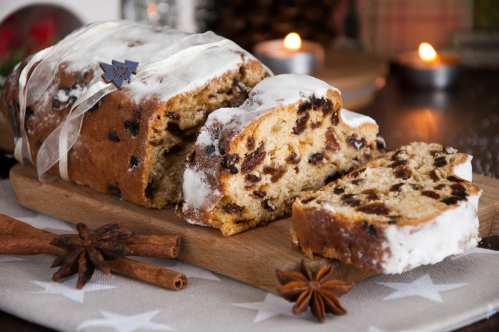 Aufgeschnittener Dresdner Christstollen mit Puderzuckerschicht, Rosinen und Gewürzen auf einem Holzbrett in weihnachtlicher Dekoration.