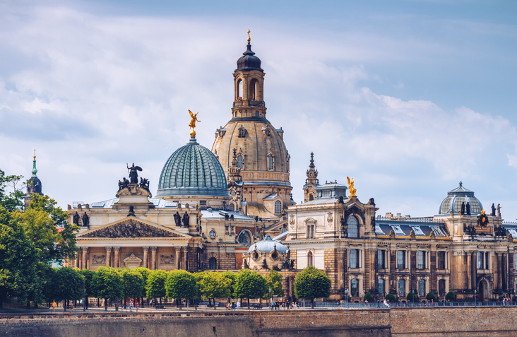 Historische Gebäude an der Brühlschen Terrasse in Dresden mit Kuppeln, Türmen, reich verzierten Fassaden und grünen Bäumen am Elbufer.