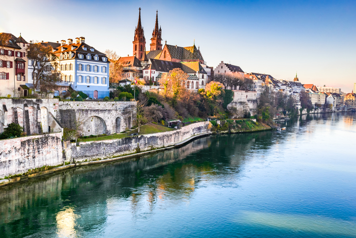 Basler Münster mit seinen beiden Türmen oberhalb des Rheins, umgeben von historischen Häusern und alten Stadtmauern.