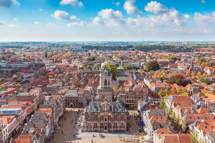 Das historische Rathaus von Delft steht auf einem großen Platz, umgeben von roten Dächern und dicht bebauter Altstadt.