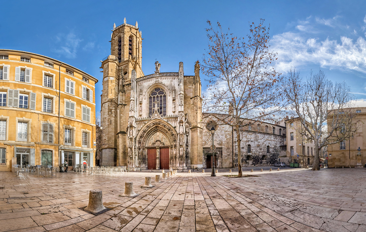 Eine historische Kirche mit verzierter Fassade steht an einem offenen Platz in Aix-en-Provence.