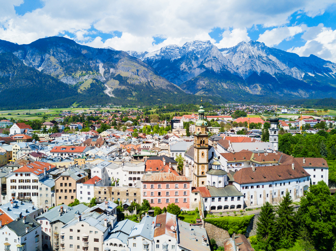 Stadtansicht von Hall in Tirol mit Kirchen, Klosteranlage und schroffen Bergen unter wolkigem Himmel.