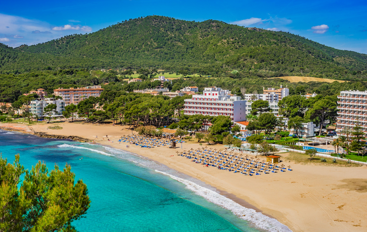 Sandstrand von Canyamel mit türkisblauem Meer, Hotels und grünem Hügel im Hintergrund