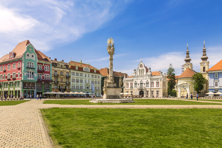 Platz mit Denkmal, Grünfläche und farbigen Fassaden in Timișoara