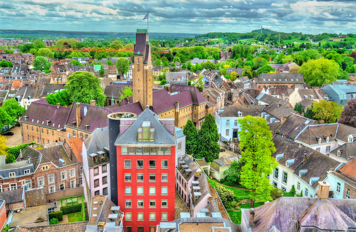 Luftaufnahme von Maastricht mit dicht bebauter Altstadt, Kirchturm, farbigen Häusern und viel Grün in der Umgebung.